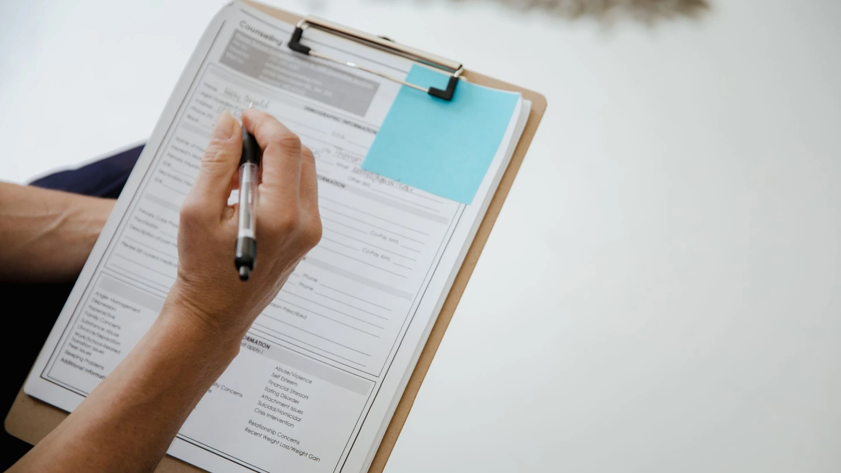 Hand filling out a paper form on a clipboard, representing manual admin work that automation and AI can replace